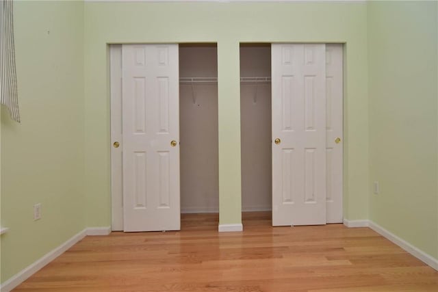 unfurnished bedroom featuring multiple closets, light wood-type flooring, and baseboards