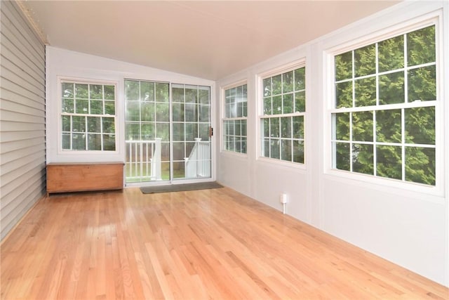 unfurnished sunroom featuring wood finished floors, vaulted ceiling, plenty of natural light, and a wooden deck