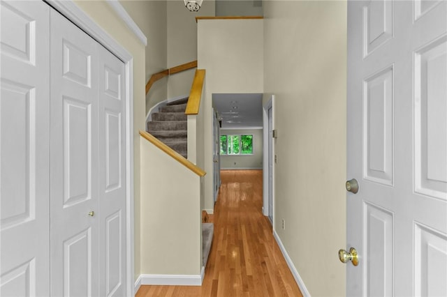 corridor with light wood finished floors, baseboards, and stairway