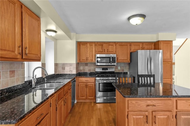kitchen with stainless steel appliances, a sink, light wood finished floors, dark stone counters, and tasteful backsplash