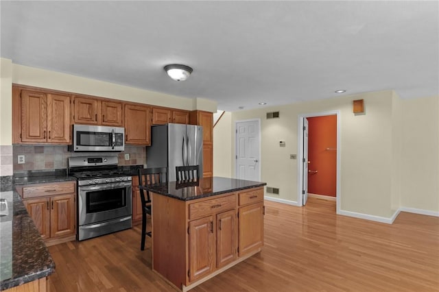 kitchen with stainless steel appliances, light wood finished floors, baseboards, a kitchen island, and tasteful backsplash