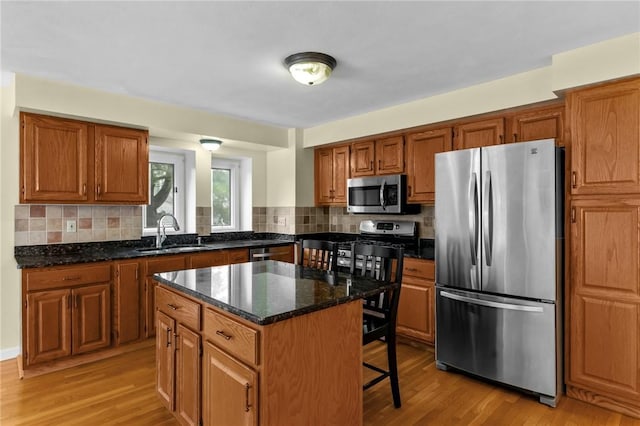 kitchen featuring appliances with stainless steel finishes, a sink, light wood-style floors, and backsplash