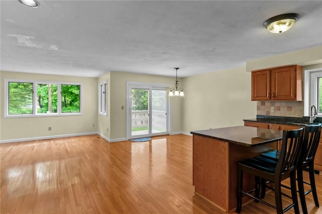 kitchen featuring a chandelier, light wood-style flooring, baseboards, brown cabinets, and decorative backsplash