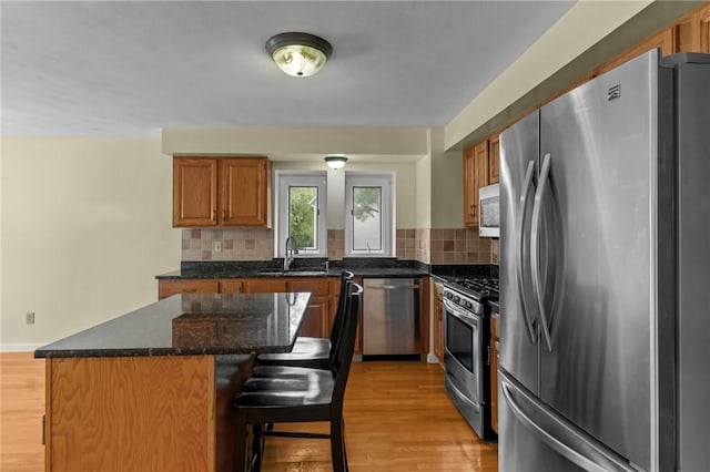 kitchen with stainless steel appliances, a sink, a center island, light wood finished floors, and tasteful backsplash