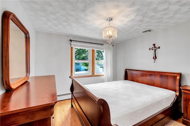 bedroom with light wood-style flooring, a baseboard heating unit, a chandelier, and a textured ceiling
