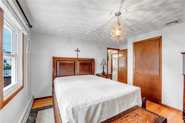 bedroom with a baseboard radiator, a chandelier, light wood-style floors, and baseboards