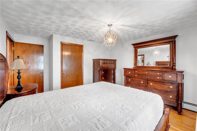 bedroom featuring light wood-style floors, a chandelier, and a baseboard radiator