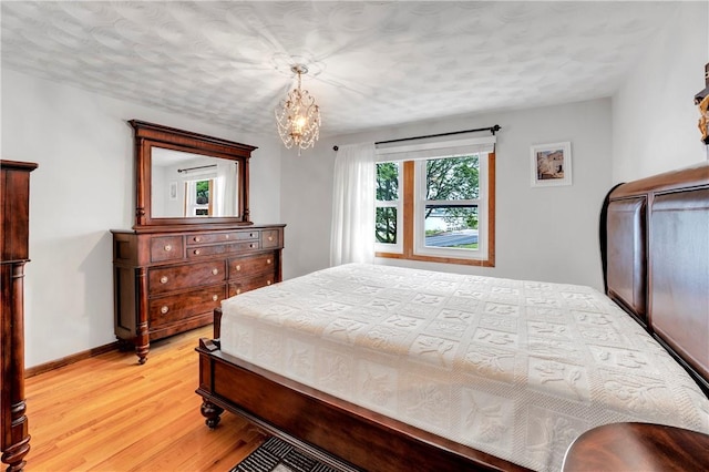 bedroom with light wood-type flooring, a chandelier, and baseboards