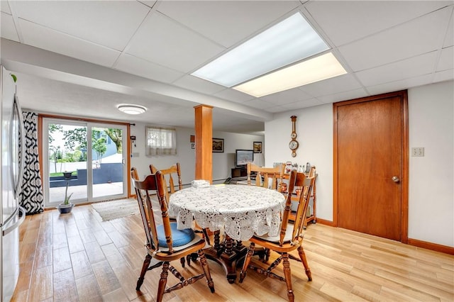 dining room featuring light wood-type flooring, a paneled ceiling, and baseboards