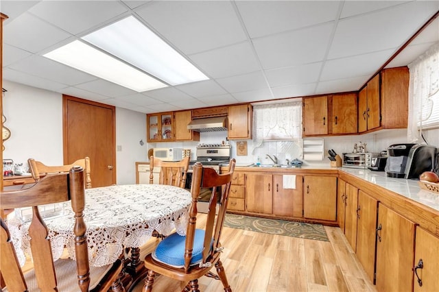 kitchen with light wood-style floors, white microwave, brown cabinets, ventilation hood, and a sink