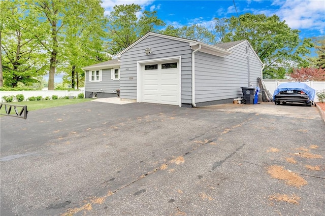 view of property exterior featuring an attached garage, fence, and driveway