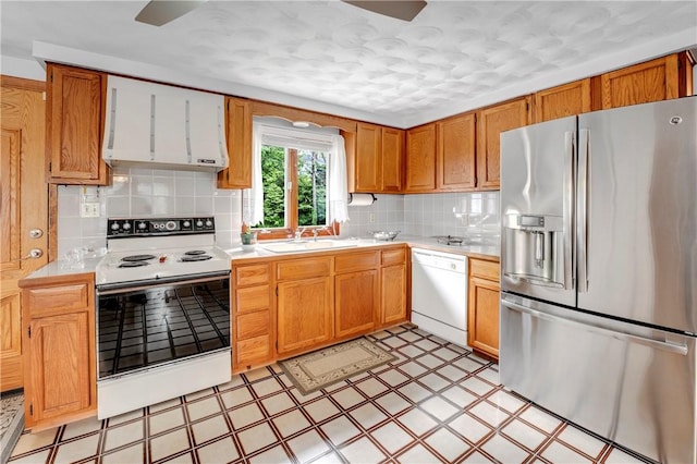 kitchen with white appliances, a sink, wall chimney range hood, light flooring, and light countertops