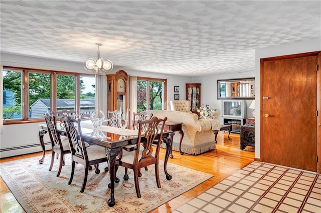 dining room featuring a chandelier, light wood-style flooring, baseboard heating, and a textured ceiling