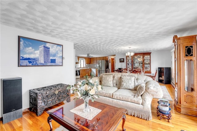 living area with healthy amount of natural light, a chandelier, light wood-type flooring, and baseboards
