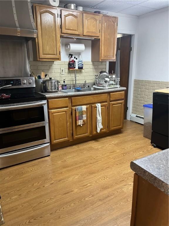 79 Dewey St, Woonsocket, RI 02895 - kitchen with double oven range, wall chimney exhaust hood, light wood-type flooring, a baseboard radiator, and backsplash