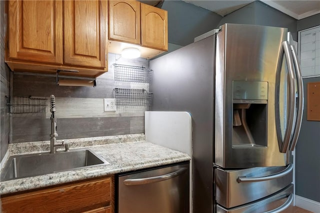 kitchen with appliances with stainless steel finishes, a sink, tasteful backsplash, light stone countertops, and brown cabinetry