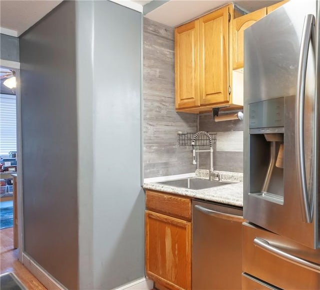 kitchen with stainless steel appliances, a sink, decorative backsplash, baseboards, and wood finished floors