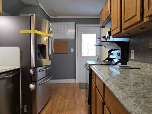 kitchen with appliances with stainless steel finishes, brown cabinets, light wood-type flooring, and light stone counters