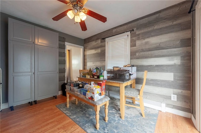office space featuring wooden walls, ceiling fan, light wood-type flooring, and baseboards