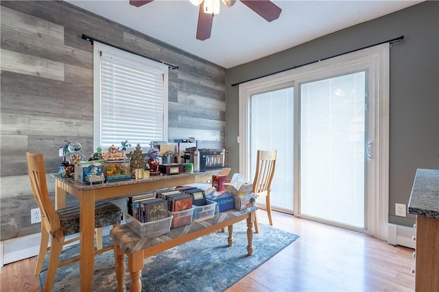 dining room featuring wood walls, an accent wall, ceiling fan, and wood finished floors