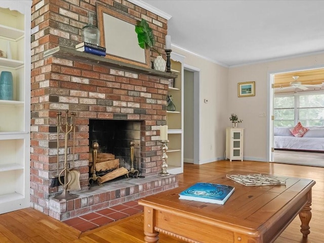 living area featuring crown molding, wood finished floors, built in features, baseboards, and a brick fireplace