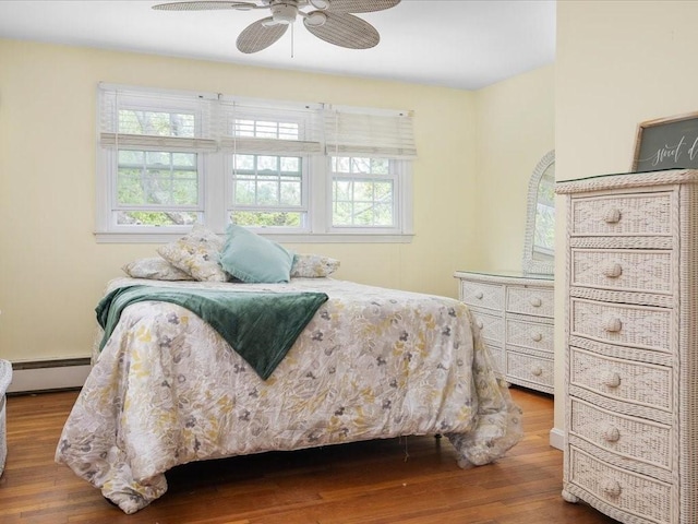 bedroom with baseboard heating, wood finished floors, multiple windows, and ceiling fan