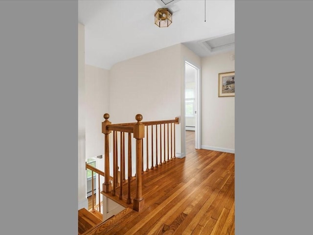 hallway with an upstairs landing, light wood-type flooring, attic access, baseboards, and baseboard heating
