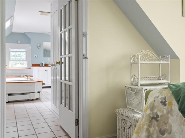 hallway with a baseboard radiator, vaulted ceiling, and light tile patterned flooring