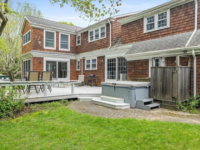 back of house with a hot tub, a wooden deck, a lawn, a shingled roof, and outdoor dining space