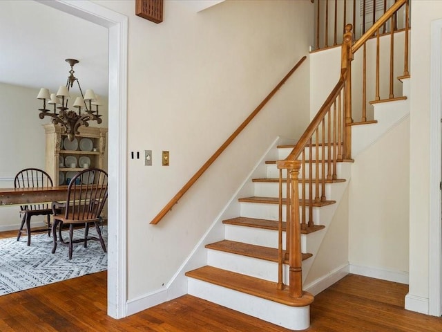 staircase with wood finished floors, baseboards, and a chandelier