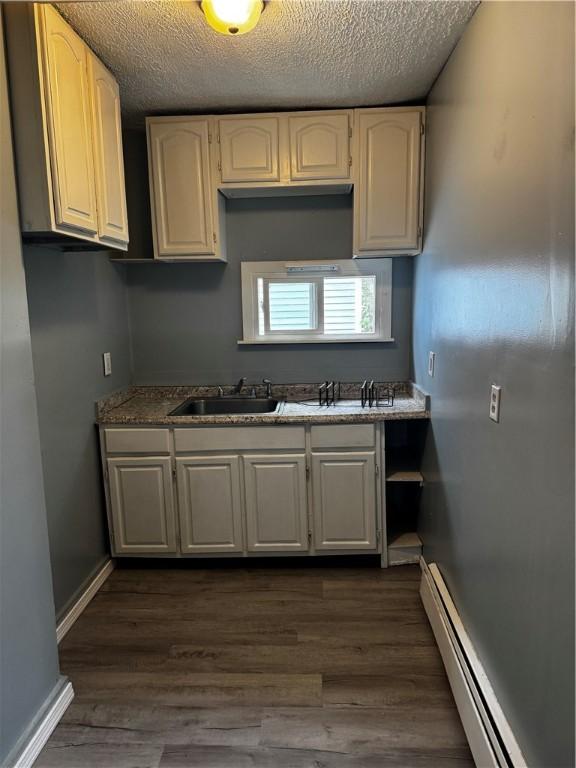 342 Paradis Ave, Woonsocket, RI 02895 - kitchen featuring a sink, baseboard heating, a textured ceiling, dark wood-style floors, and baseboards