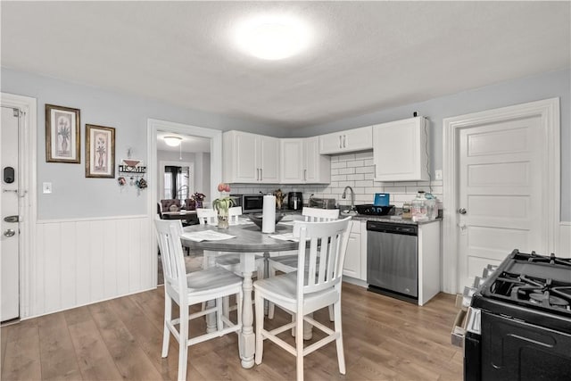 kitchen with appliances with stainless steel finishes, white cabinets, a wainscoted wall, light wood-type flooring, and decorative backsplash