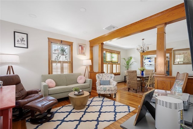 living area featuring ornate columns, a chandelier, and wood finished floors