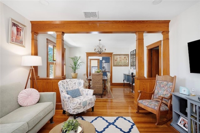 sitting room with ornate columns, a chandelier, and light wood-style flooring