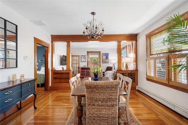 dining room with a baseboard radiator, decorative columns, light wood-style floors, and a chandelier