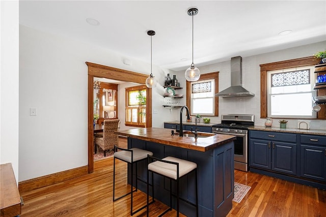 kitchen featuring wall chimney exhaust hood, stainless steel gas range oven, wood counters, a sink, and blue cabinets