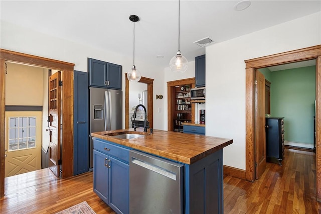 kitchen with appliances with stainless steel finishes, a sink, blue cabinetry, dark wood-style flooring, and butcher block countertops