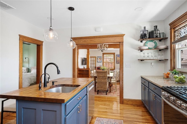 kitchen with wooden counters, blue cabinets, a sink, appliances with stainless steel finishes, and light wood-type flooring