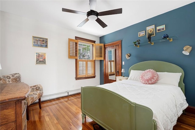 bedroom featuring wood finished floors, a baseboard heating unit, and ceiling fan