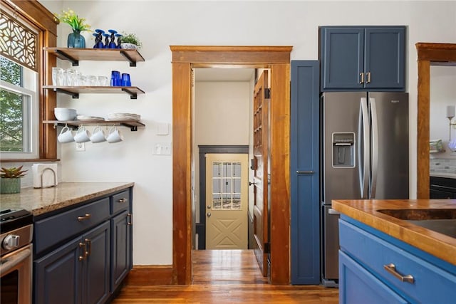 kitchen with stainless steel appliances, wood finished floors, blue cabinets, and light stone countertops