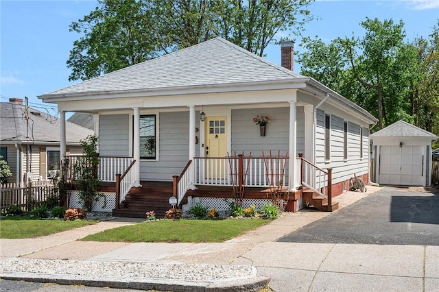 view of front of home with a chimney, an outbuilding, roof with shingles, covered porch, and a detached garage