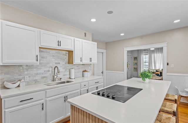 kitchen with a sink, black electric cooktop, wainscoting, white cabinets, and a center island