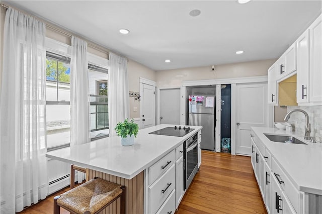 kitchen with appliances with stainless steel finishes, a sink, white cabinets, light countertops, and a kitchen island
