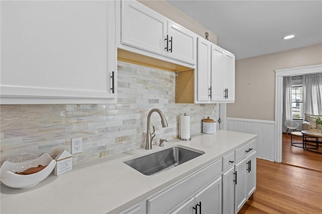 kitchen with a sink, light countertops, white cabinets, light wood-type flooring, and wainscoting