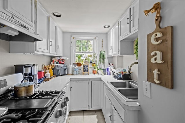 kitchen with under cabinet range hood, a sink, gas range, light tile patterned flooring, and white cabinets