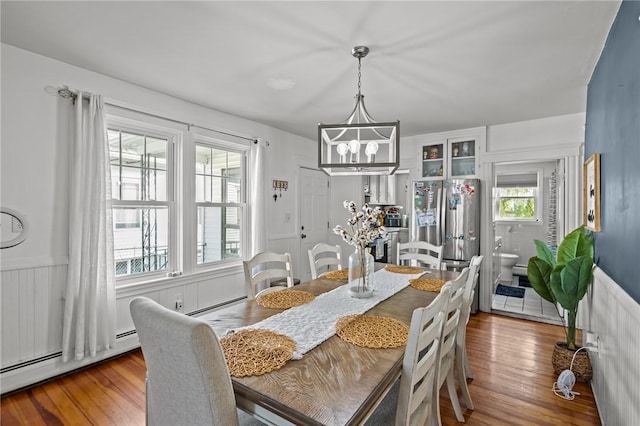 dining area featuring wood finished floors, a chandelier, baseboard heating, and a wainscoted wall