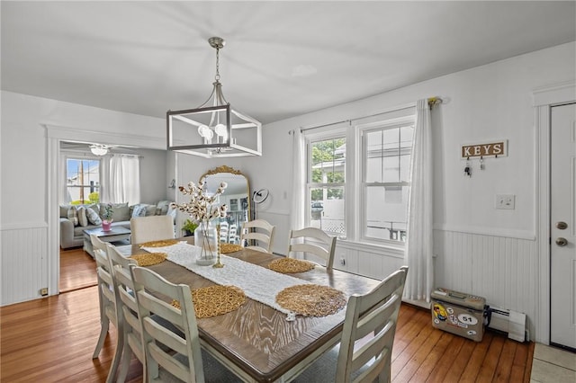 dining room featuring a wainscoted wall, hardwood / wood-style floors, a chandelier, a baseboard radiator, and wooden walls