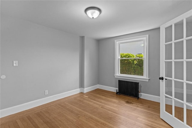 empty room featuring radiator, baseboards, and light wood-type flooring