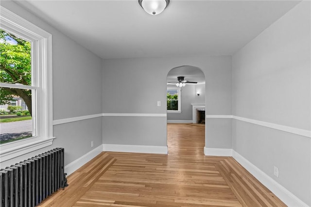 spare room featuring radiator, ceiling fan, light wood-type flooring, and baseboards