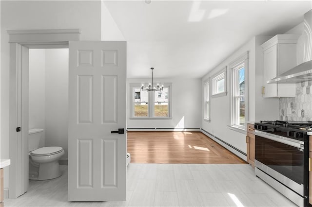 1314 Chalkstone Ave, Providence, RI 02908 - kitchen with gas stove, a baseboard radiator, a chandelier, wall chimney range hood, and white cabinetry